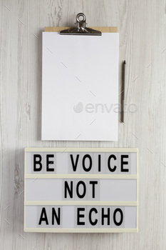 'Be voice not an echo' on a lightbox, clipboard with blank sheet of paper on a white wooden surface