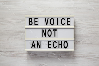 'Be voice not an echo' on a lightbox on a white wooden surface, top view.