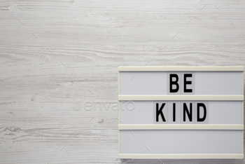 'Be kind' on a lightbox on a white wooden surface, top view. Flat lay, overhead, from above.