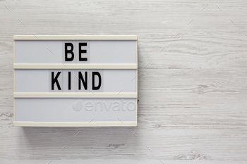 'Be kind' on a lightbox on a white wooden background, top view. Flat lay, overhead, from above.