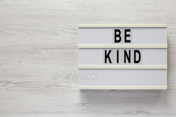 'Be kind' on a lightbox on a white wooden surface, top view. Flat lay, overhead, from above.