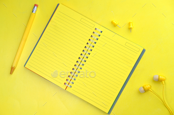 notebook, pencils and headphone on yellow background