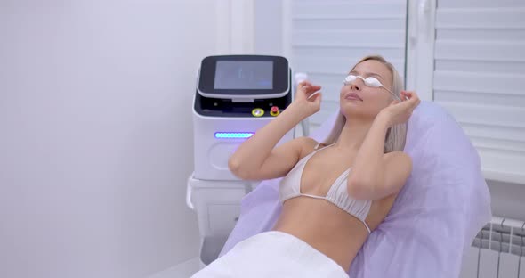 Young Woman in a Swimsuit and Protective Cosmetic Glasses Lies in the Cosmetologist’s Office on