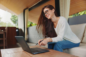 A Smiling Woman Working from Home with Her Laptop on the Sofa