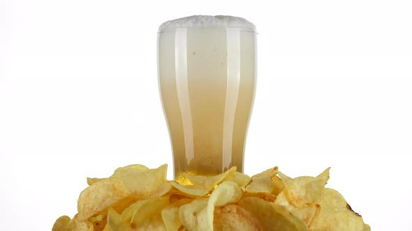 pouring beer in glass, potatoes chips around. foam in a glass of beer