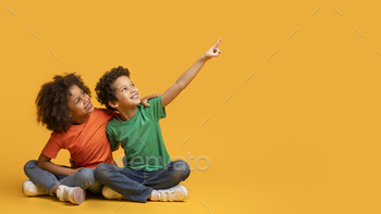 Two Children Sitting on Yellow Background Pointing