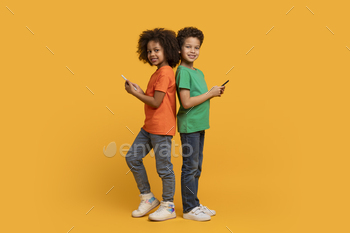 Two Children Holding Cell Phones on Yellow Background