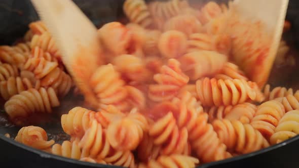 Stir pasta fusilli and tomato sauce in pan, close up