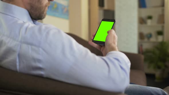Bearded Male Sitting on Sofa and Scrolling on Cellphone With Green Screen, App
