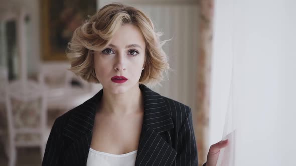 Portrait of Stylish Woman in Suit Looks Through the Light Window and Aside