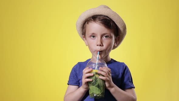 Cute boy Drinking Mojito cocktail From Plastic Cup Over Yellow Studio Background