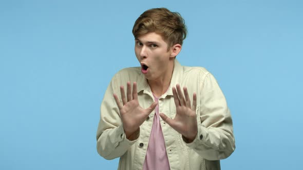 Image of Shocked and Worried Young Man Showing Slow Down Gesture Raising Hands and Asking to Calm