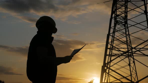 Silhouette of Engineer Standing on Field with Electricity Towers. Electrical Engineer with High