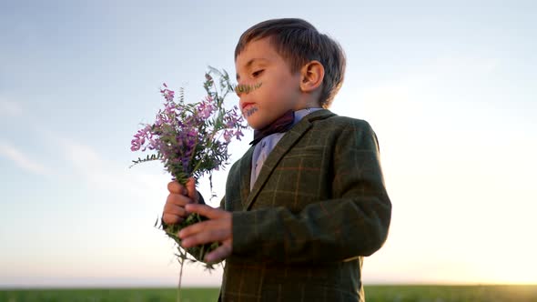 Portrait of Cute Little Boy in Festive Costume with Butterfly and Bouquet on Open Area Field