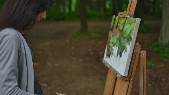 Female's Hand Painting a Landscape on Canvas in a Park.