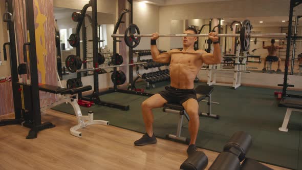A Young Bodybuilder Training in the Gym and Does a Barbell Press From the Chest Sitting While