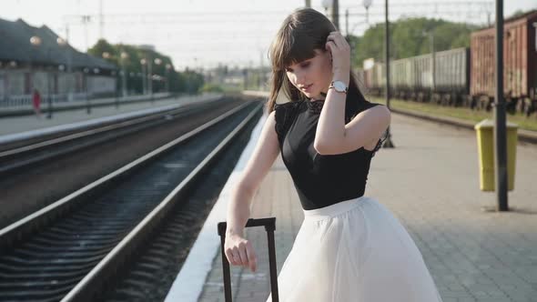 Attractive Model Smiling, Poses with Lush Skirt at Suitcase on Railway Platform