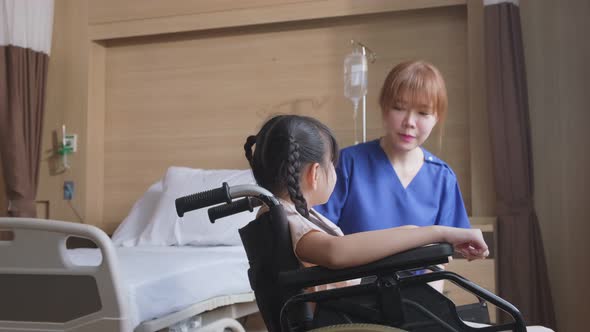 Asian nurse taking care of little girl kid patient sit on wheelchair in recovery room in hospital.