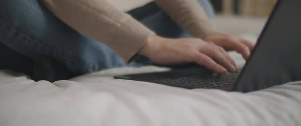 Man hands typing something on a laptop keyboard in the bedroom.