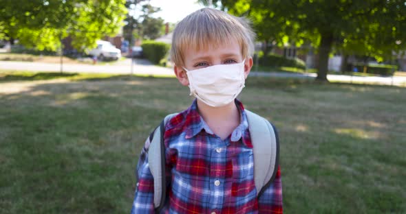 Little boy takes off his face mask in a school yard.