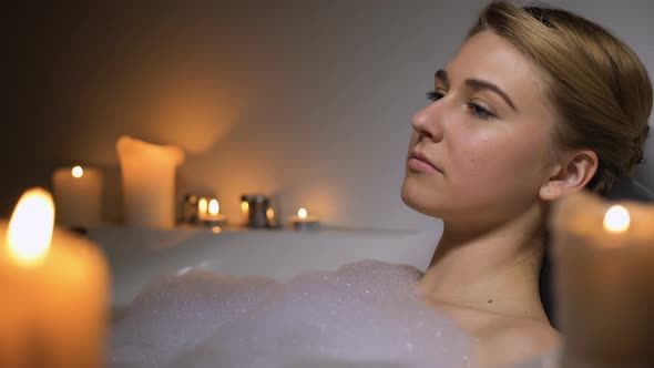 Pensive Woman Lying in Bath With Foam Bubbles and Candles, Thinking About Life