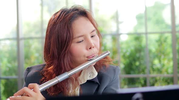 Asian woman teacher in business suit she teaches classical music Playing the flute