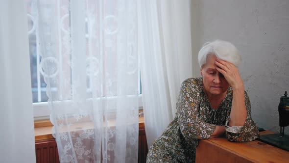 Greyhaired Caucasian Grandmother Sitting Alone During Grandparent's Day and Touching Her Head