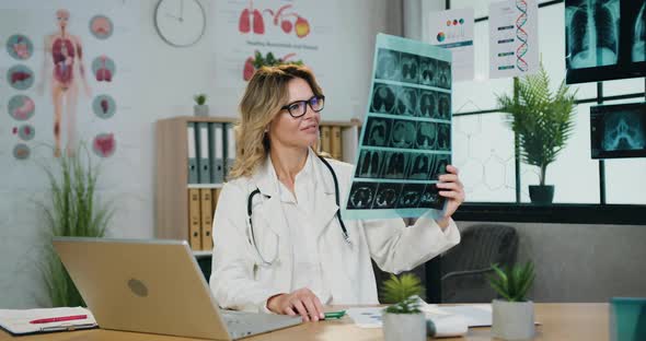 Female Doctor in Glasses Filling Medical Card on Laptop Using Results of X-ray Scan