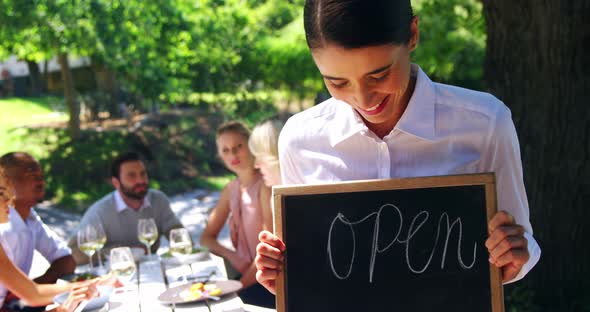 Smiling waitress showing chalkboard with open sign