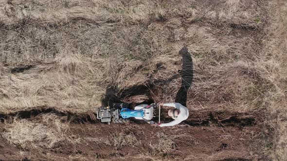 AERIAL - Man working a field with a rototiller, agriculture, wide shot pan left