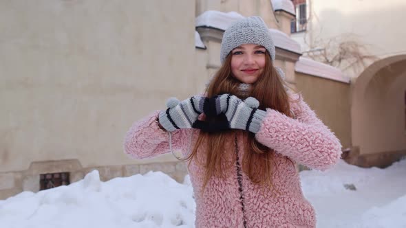 Caucasian Young Woman Smiling to Camera Showing Heart Sign While Standing Outdoor in Winter City