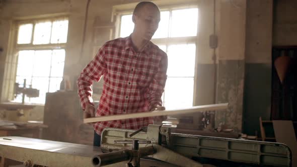 Concentrated Caucasian Bolding Male in Red Plaid Shirt Putting Long Wood Plank on Jointer Machine in