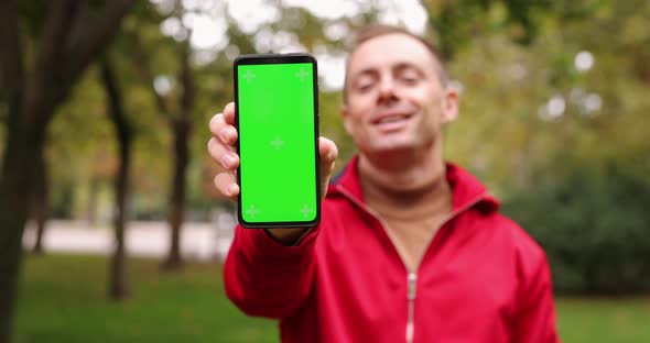 Man Showing Green Screen of Smartphone in a Park