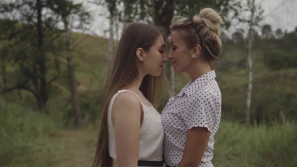 Middle Shot Side View of Adult and Young Caucasian Women Standing with Heads Together Outdoors