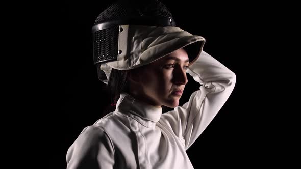 Side View of Young Woman Fencer Puts Sports Mask Helmet