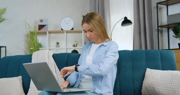 Female Student in Casual Clothes Sitting on Couch at Home and Working on Laptop
