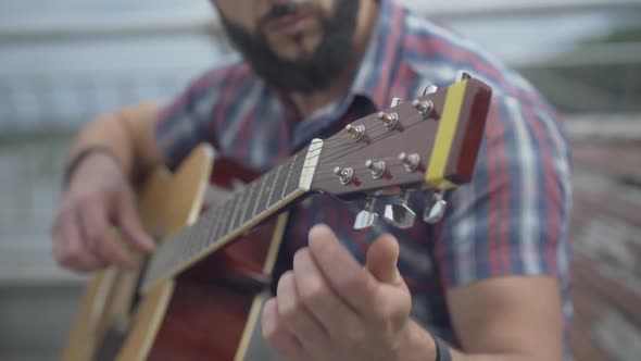 Close-up of Guitar Fingerboard with Blurred Bearded Man Playing Musical Instrument. Unrecognizable