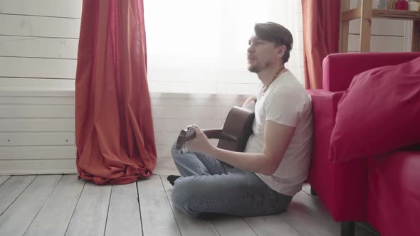 A Man Sits on the Floor Plays the Guitar at Home and Sings