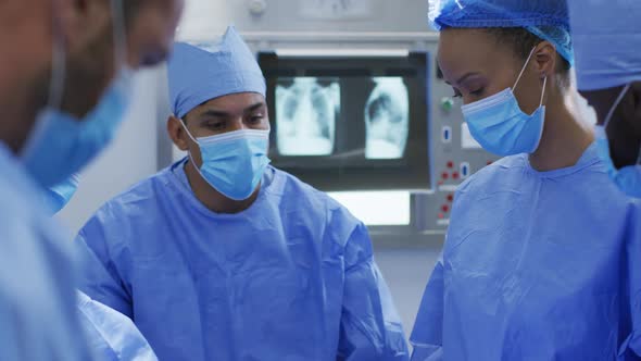 Mixed race surgeons wearing protective clothing discussing in operating theatre