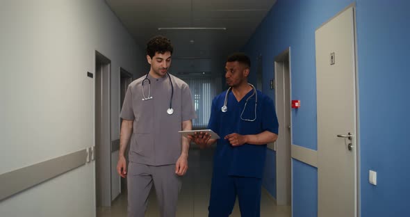 A Doctor Shows His Colleague Information on a Tablet in the Corridor of Clinic