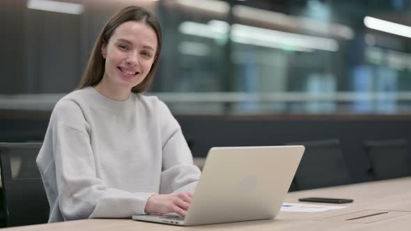 Woman Smiling at Camera while working on Laptop