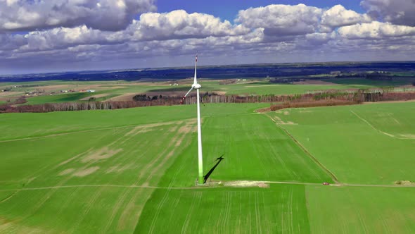 Aerial view of white wind turbine on green field in spring