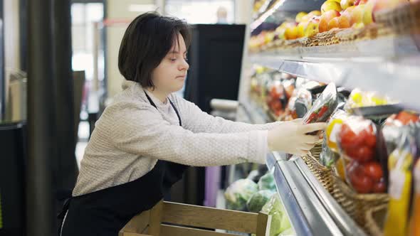 Female Worker with Down Syndrome Restocking Vegetables From the Box