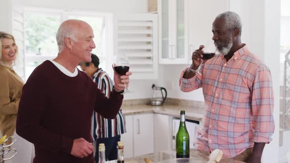 Diverse senior couples drinking wine and preparing vegetable salad in a kitchen