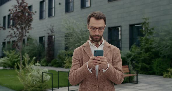 Crop View of Serious Guy in Stylish Clothes Using Smartphone and Looking Aside