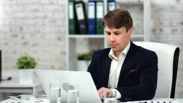 Male Confident Office Worker Wearing Suit Typing on Laptop Looking at Screen at Workplace