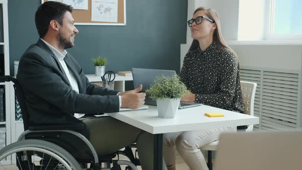 Disabled Guy in Wheelchair Discussing Business with Female Colleague Talking Sitting at Desk in