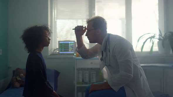 Physician Testing Pupil Reflex Shining Flashlight in African American Girl Eyes