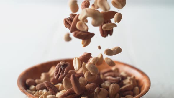 Camera follows peanuts, pecans and cashew nuts falling into a bowl. Slow Motion.