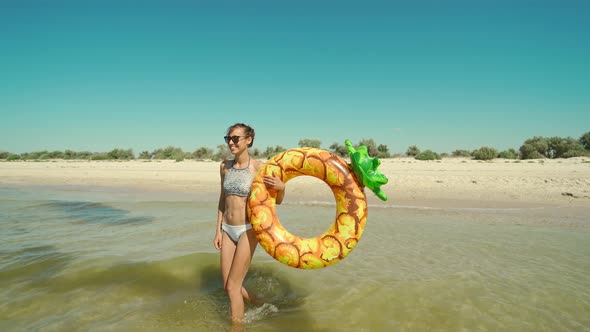 Portrait of Happy Smiling Young Woman in Sunglasses with Inflatable Pineapple Ring Walks in Sea